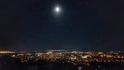 a view of a city at night with the moon at Apartamento con vistas al mar in Viladecáns