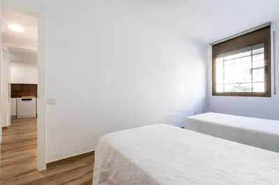 a white bedroom with two beds and a window at Macu in Sabadell