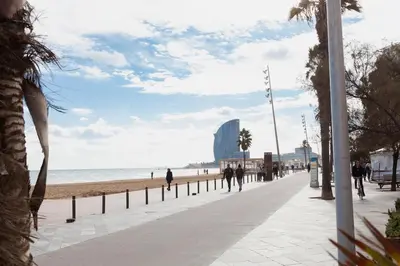 a beach with people walking down a sidewalk at Barceloneta Mar Beach - BM32 in Barcelona
