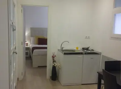a white kitchen with a sink and a room with a bed at BruStar Sagrada Familia in Barcelona