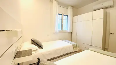 a white bedroom with two beds and a window at Apartamento familiar by prestigi in Terrassa