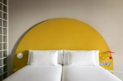 two beds in a room with a yellow wall at BYPILLOW Flamant in Barcelona