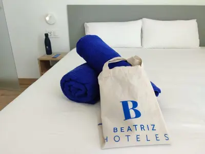 a blue teddy bear with a tote bag on a bed at Hotel Calella by Beatriz Hoteles in Calella