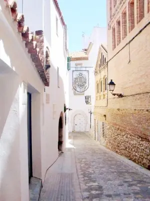 an alley with buildings and a clock on the wall at Pis Sitges centre in Sitges