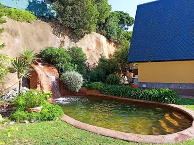 a pond in front of a house with a waterfall at Villa cascada in Sant Cebrià de Vallalta