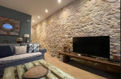 a living room with a stone wall with a flat screen tv at Rustic Casita Gavà in Barcelona