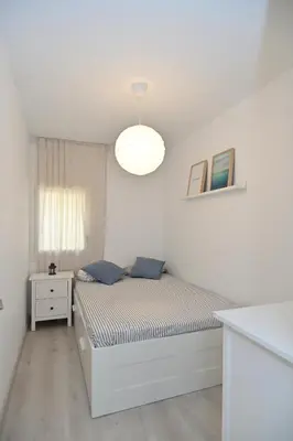 a white bedroom with a bed and a table at Apartamento con piscina en Sant Pol de Mar in San Pol de Mar