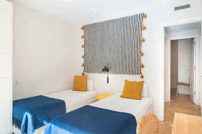 two beds in a white room with blue and yellow pillows at Spacious and elegant oasis in the best location, Eixample Barcelona in Barcelona