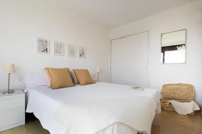 a white bedroom with a large bed and a chair at Bright Apartment In Gava Mar in Gavà