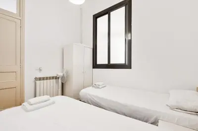 two beds in a white room with a window at 5BR for 7 Elevator Walk to Sant Antoni in Barcelona