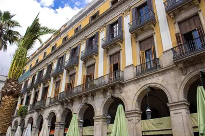 a large yellow building with balconies and a palm tree at Hostal Ambos Mundos in Barcelona