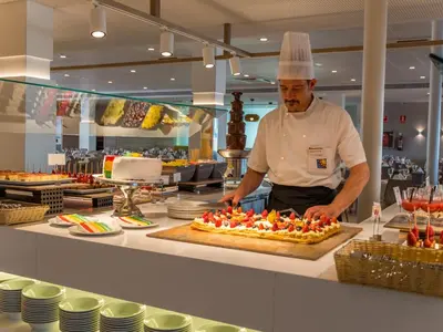 a chef standing in a kitchen preparing a cake at Golden Taurus Aquapark Resort in Pineda de Mar