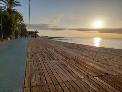 a boardwalk on the beach with the sun setting at Oasis cerca de Barcelona in Sant Vicenç de Montalt