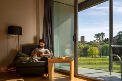 a man sitting in a chair in a living room with a book at Hotel Món Sant Benet in Sant Fruitos de Bages
