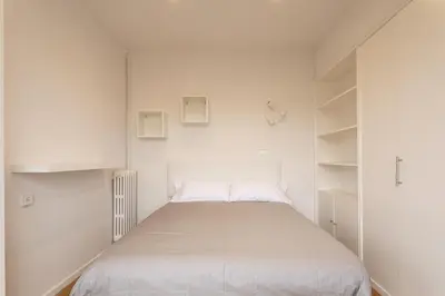 a small white bedroom with a bed and shelves at Gran Vía Suites in Barcelona