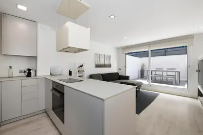 a kitchen with white cabinets and a living room at Namasté by Seaside Homes in Castelldefels