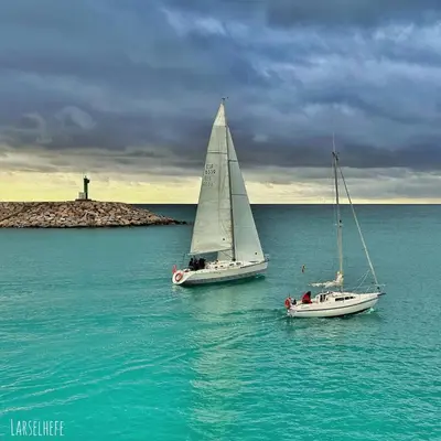 two sailboats in the water with a lighthouse in the background at Habitación premium in Vilanova i la Geltrú