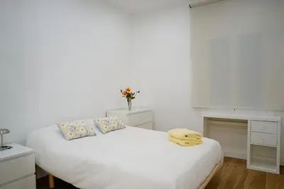 a white bedroom with a white bed with blue pillows at Apartamentos Valentin in Barcelona