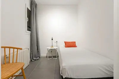 a white bedroom with a bed and a chair at Flateli Espronceda 22 in Barcelona