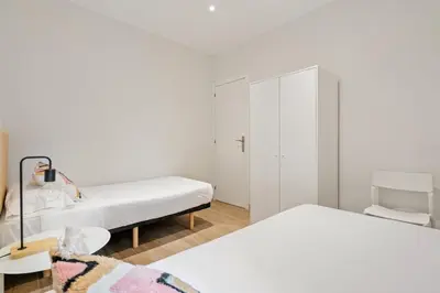 a white bedroom with two beds and a cabinet at Flateli Espronceda 32 in Barcelona