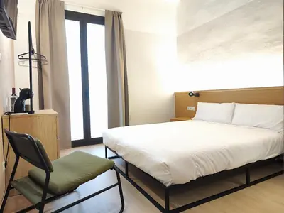 a bedroom with a bed and a chair and a window at Mazi Plaça Gran in Mataró