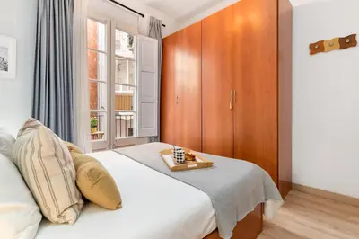 a bedroom with a white bed with a wooden cabinet at Whisper-Quiet 2BR Near Sagrada in Barcelona