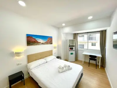 a white bedroom with a bed and a desk at Lux Hostal in Hospitalet de Llobregat