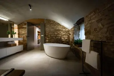 a bathroom with a tub and a stone wall at Villa Mas Summit in Collsuspina