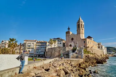 a person standing on a wall near the water with a church at Francesc Macià, Sitges in Sitges