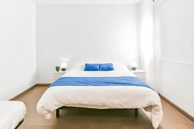 a white bedroom with a large bed with blue pillows at Laramond Barcelona Rooms in Barcelona