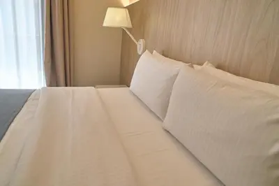 a white bed with white pillows and a lamp at Hotel Omnium in Barcelona