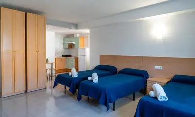 a room with three blue beds and a kitchen at Apartaments Turístics Residencia Vila Nova in Vilanova i la Geltrú