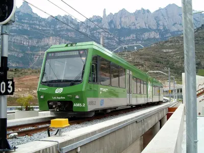 a green train on tracks with mountains in the background at Apartments Mo in Monistrol