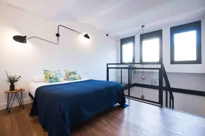 a bedroom with a bed with blue sheets and windows at Magatzem 128 in Barcelona