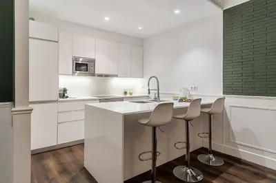 a kitchen with white cabinets and a sink and stools at Enjoybcn Tallers Apartment in Barcelona