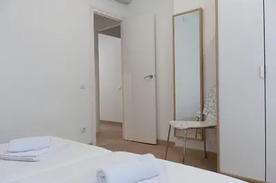 a white bedroom with a mirror and a chair at Flateli Roger 6 in Barcelona