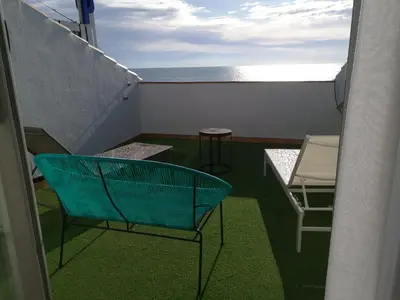 a balcony with a blue chair and chairs and the ocean at Vila De Premiá in Premiá de Mar