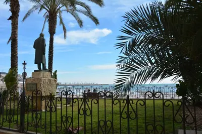 a statue of a man behind a fence with palm trees at Apartamento Flavia II Sant Damià in Sitges