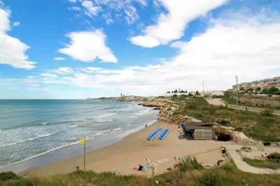 a beach with blue lounge chairs and the ocean at Casa Cala Balmins in Sitges