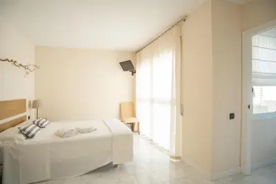 a white bedroom with a bed and a window at Casa Cala Balmins in Sitges