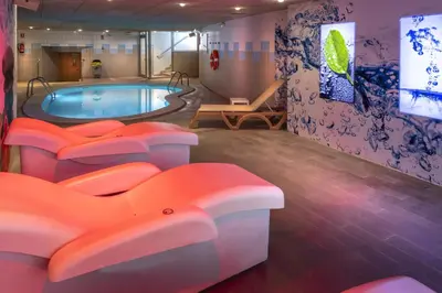 a room with a swimming pool with orange chairs around it at GHT Maritim in Calella