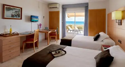 a hotel room with two beds and a desk at Aparthotel Solifemar in Castelldefels