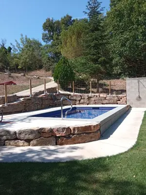 a swimming pool with a stone wall and a fountain at Entre Roures in Moià
