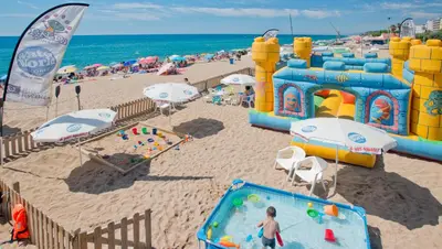 a beach with people playing in the sand and a playground at Hotel Sorrabona in Pineda de Mar