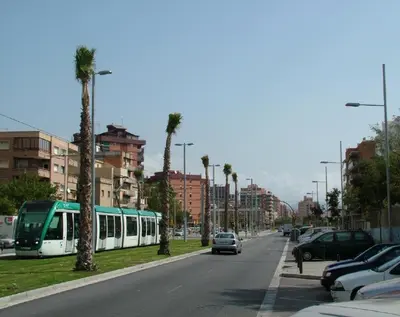 a green and white train on a city street with palm trees at LG Big Flat Barcelona in Badalona