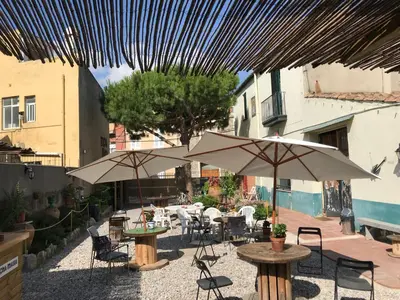 an outdoor patio with tables and chairs and umbrellas at Mucha Masia Hostel Rural Urba in El Prat de Llobregat