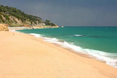 a sandy beach with the ocean and green water at Casa Mar y Piscina (solo familias) in Sant Cebrià de Vallalta