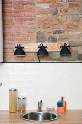 two lights above a kitchen sink in front of a brick wall at Rincón de piedra BCN in Corró de Vall
