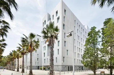 a white building with palm trees in front of it at Lugaris Beach Apartments in Barcelona