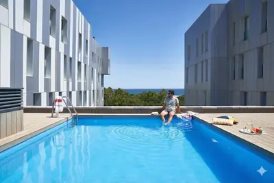 a man sitting on the edge of a swimming pool at Lugaris Beach Apartments in Barcelona